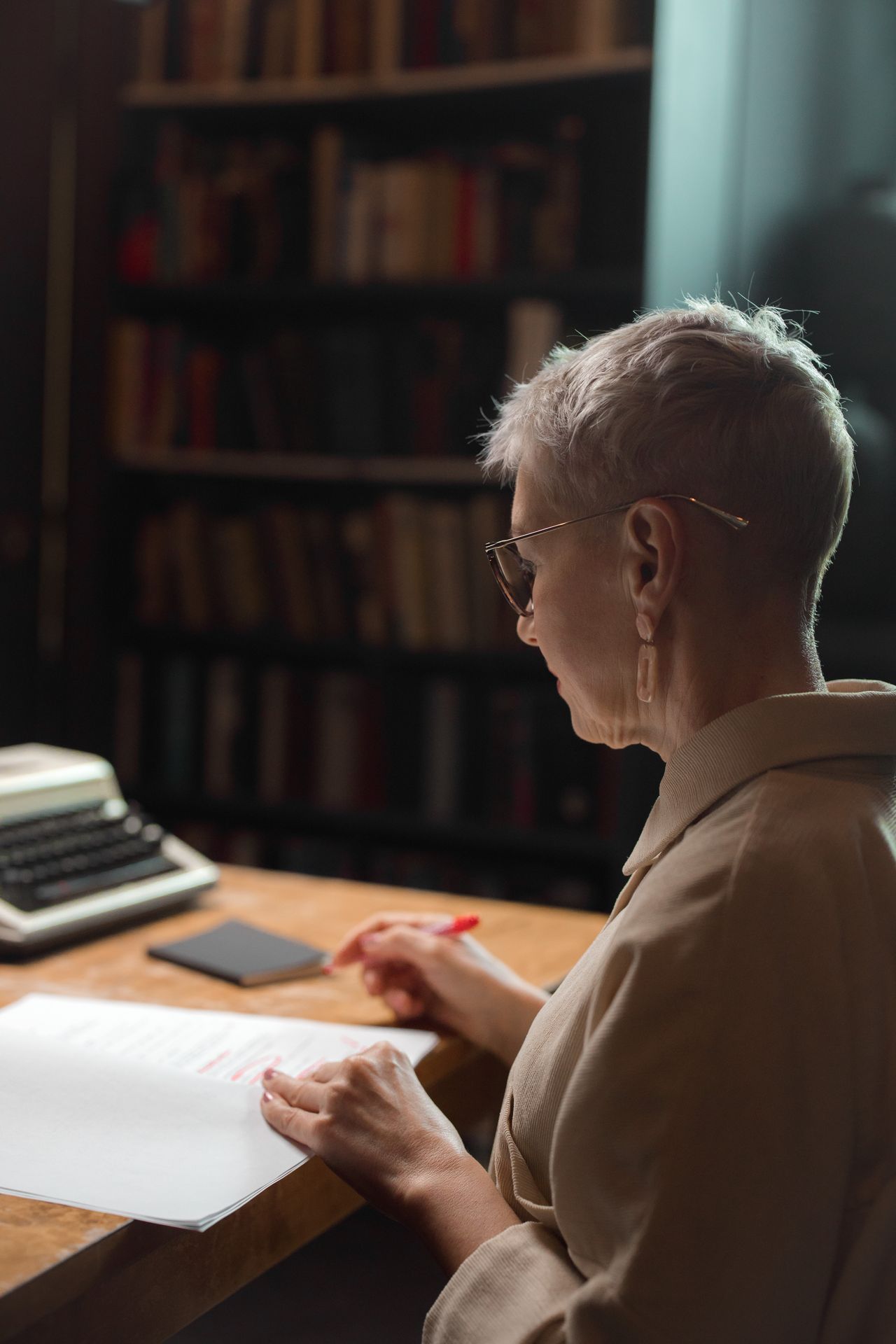 Senior woman reviewing script with red pen in library setting